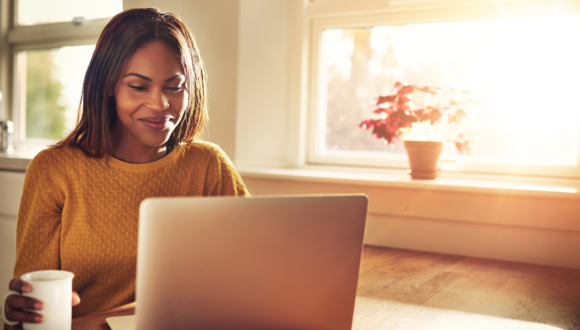 Person holding cup smiles at laptop