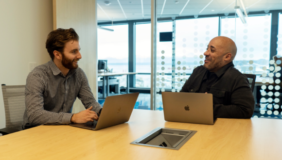 Two people with laptops smile at each other